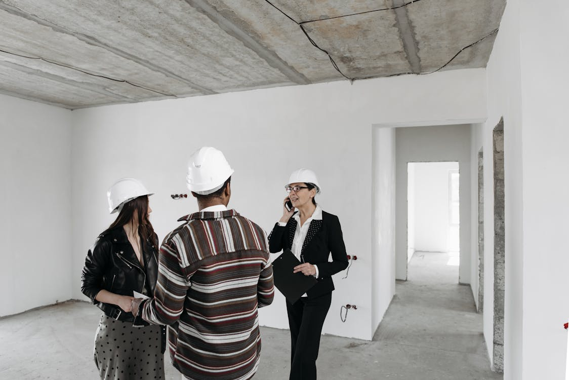 A realtor showing a house to a couple while wearing safety hats